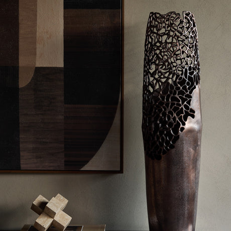 Libra Interiors Coral Cut-Out bronze aluminium floor vase with smooth base and pierced openwork top, styled beside abstract art and a travertine sculpture.