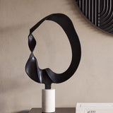 Libra Interiors Looping Abstract sculpture in matt black cast aluminium on a white marble cylindrical base, styled on a console beside a dark ridged mirror.