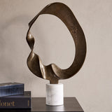 Libra Interiors Abstract Aluminium Ring Sculpture in antique gold with a looping textured form on a white marble base, styled beside books on a console.