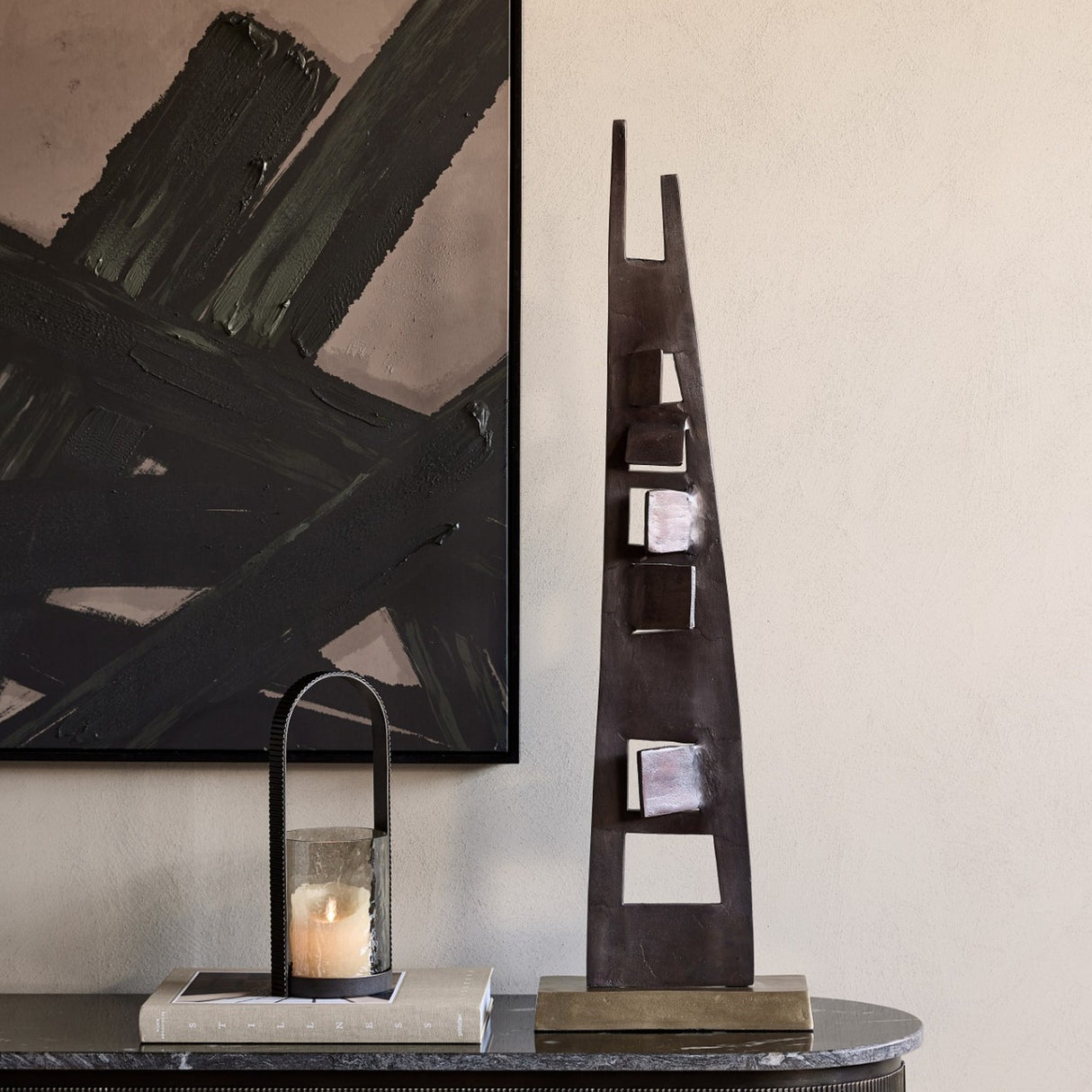 Libra Interiors tall geometric cut-out aluminium sculpture in bronze on a brass-toned base, styled on a marble console beside a lantern and abstract artwork.
