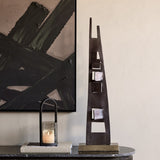 Libra Interiors tall geometric cut-out aluminium sculpture in bronze on a brass-toned base, styled on a marble console beside a lantern and abstract artwork.