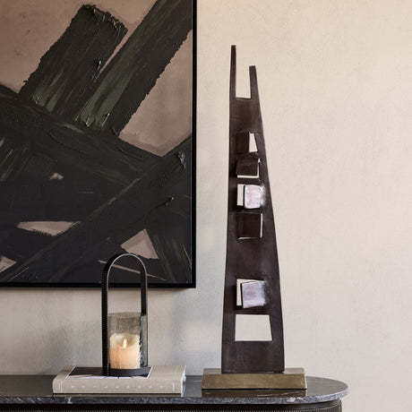 Libra Interiors tall geometric cut-out aluminium sculpture in bronze on a brass-toned base, styled on a marble console beside a lantern and abstract artwork.