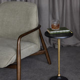 Libra Interiors Grooved Sunburst round side table with blackish bronze top and matt gold stem, styled beside an armchair with a book and whisky glass.
