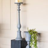 Libra Interiors Stonewashed Aluminium Pillar Candle Holder in grey, styled on a dark plinth beside a matching grey urn planter with trailing greenery.
