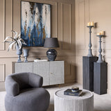 Libra Interiors Stonewash Grey Aluminium Urn Vases on a patterned sideboard with abstract blue art, table lamp and grey candlesticks in a living room.