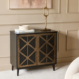 Libra Interiors embossed ceramic triple-wick candle in blue-green sits on books atop a dark cabinet with geometric bronze doors, beside a brass sculpture.