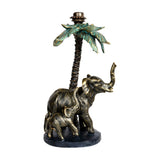 Libra Interiors gold resin candle holder with a mother elephant and calf beneath a palm tree with green fronds and taper fitting.