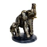 Libra Interiors Palm and Elephant resin candle holder in gold, showing a mother elephant and calf beside a palm trunk on a black base.