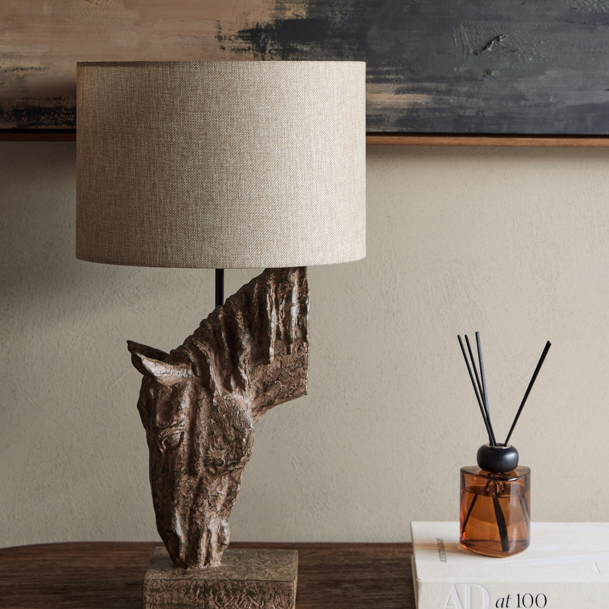 Libra Interiors Sculptural Horse Head resin table lamp in brown with weathered finish and neutral hessian-effect drum shade, styled on a wooden console.