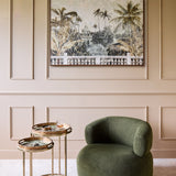 Libra Interiors Aged Palm Pavilion framed canvas wall art above a green bouclé chair and brass side tables in a panelled living room.