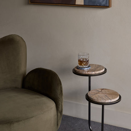 Libra Interiors Two-Tier Marble Dual-Top Side Table in bronze beside a green velvet armchair, holding a crystal whisky glass on the Forest Brown marble tier.