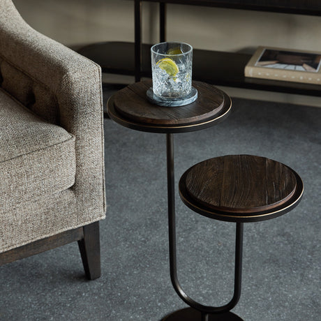 Libra Interiors Two-Tier Mango Wood Side Table in bronze beside a beige armchair, holding a crystal tumbler with lemon on a marble coaster.