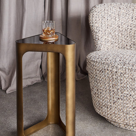 Libra Interiors Triangular Smoked Gold Iron Side Table in bronze with black tinted glass top holding a whiskey glass, beside a tweed armchair.