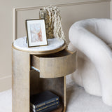 Libra Interiors Marble Top Bedside Table in gold with open drawer, ridged iron frame, white marble top styled with a photo frame and trailing foliage.