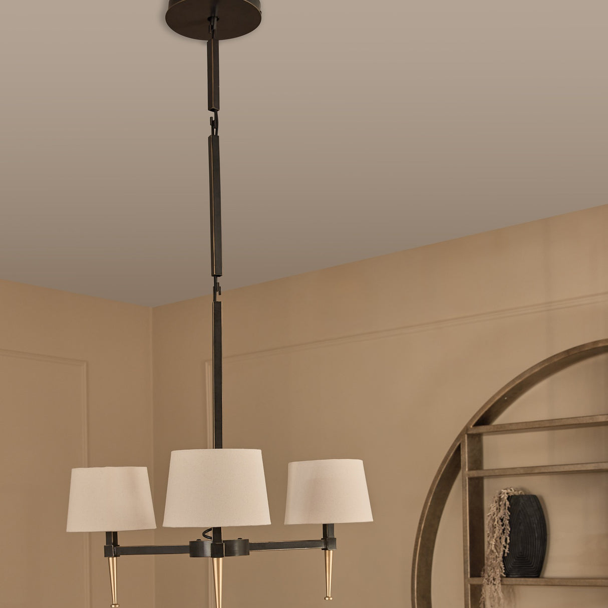 Libra Interiors 3-Light Linen Shade Bronze Chandelier with pale linen shades and gold tapered feet, hanging from an adjustable drop in a warm neutral room.