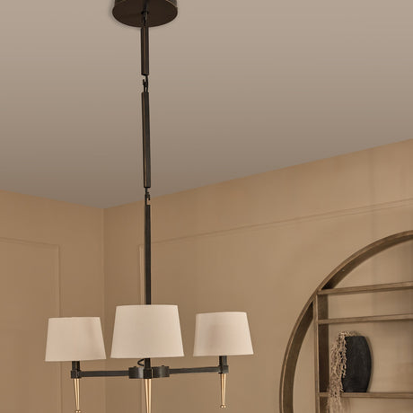 Libra Interiors 3-Light Linen Shade Bronze Chandelier with pale linen shades and gold tapered feet, hanging from an adjustable drop in a warm neutral room.