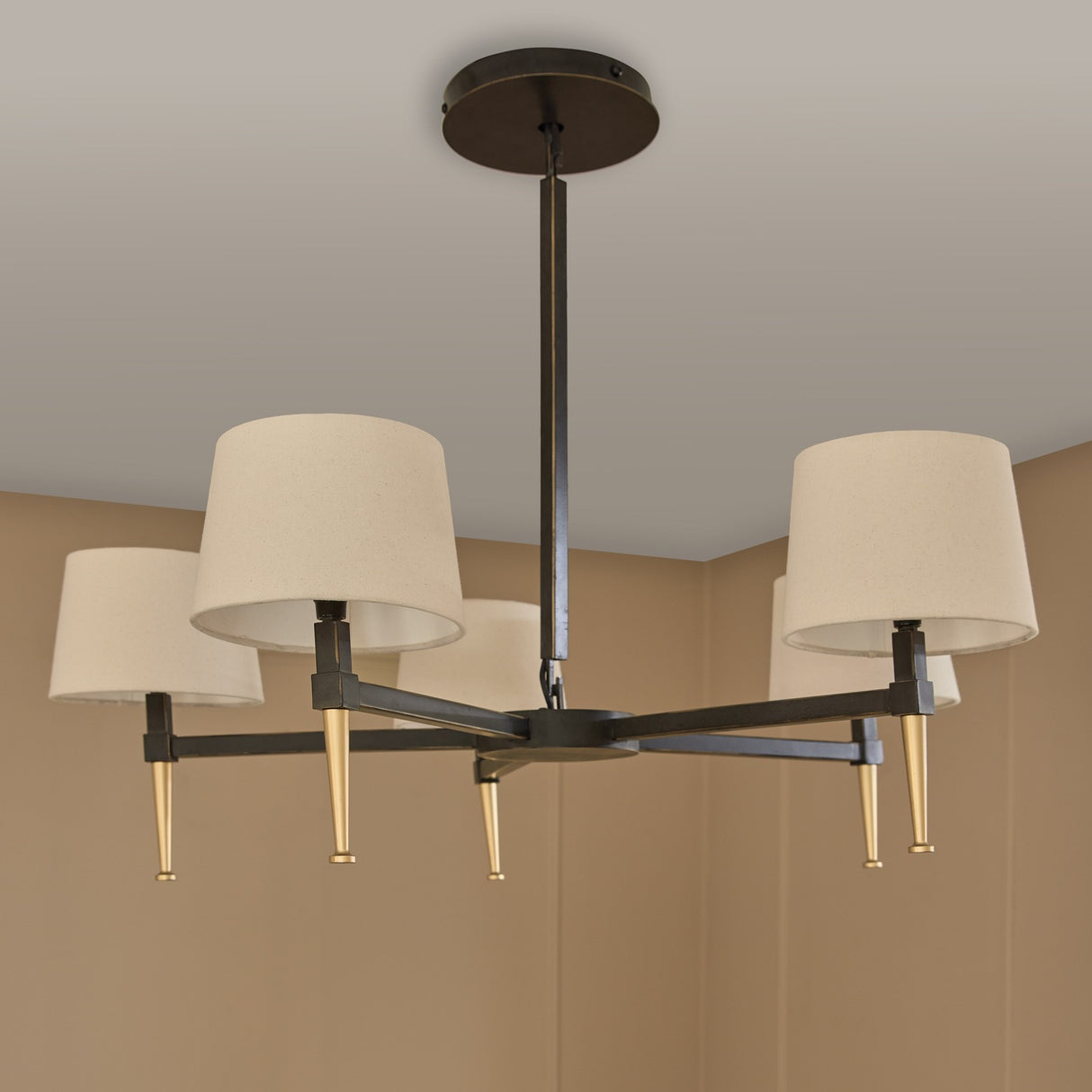 Libra Interiors Bronze Iron 5 Light Linen Chandelier with cream linen shades, bronze frame and gold tapered accents, mounted to a neutral ceiling.