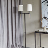 Libra Interiors Twin Shade Bronze Iron Floor Lamp with two bleached linen shades and gilded accents, styled beside grey curtains and a black console table.