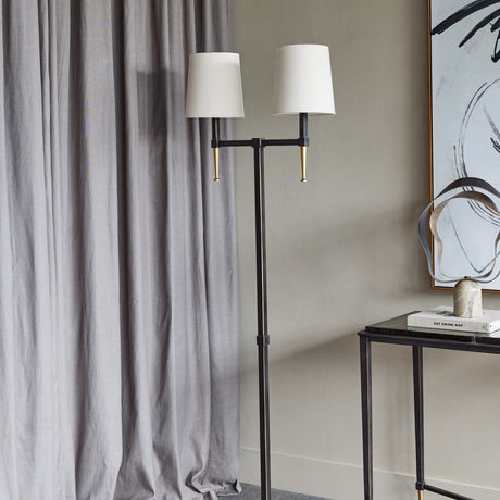 Libra Interiors Twin Shade Bronze Iron Floor Lamp with two bleached linen shades and gilded accents, styled beside grey curtains and a black console table.