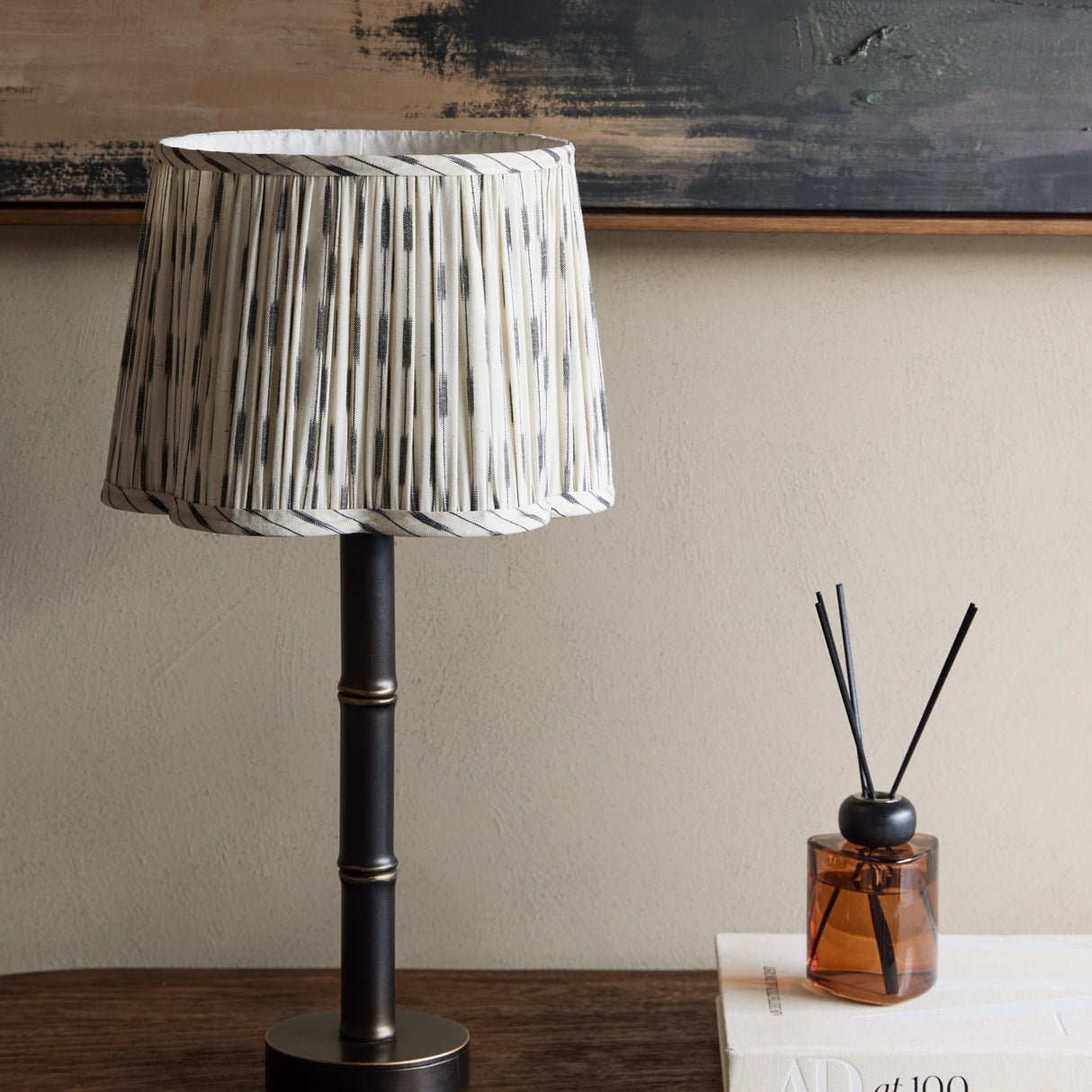 Libra Interiors Bamboo-Effect Pleated Ikat table lamp with grey and cream pleated linen shade on a dark bronze ribbed iron base, styled on a console.
