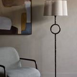 Libra Interiors Hammered Iron floor lamp in bronze with circular stem detail and scalloped linen shade, beside a grey armchair and abstract artwork.