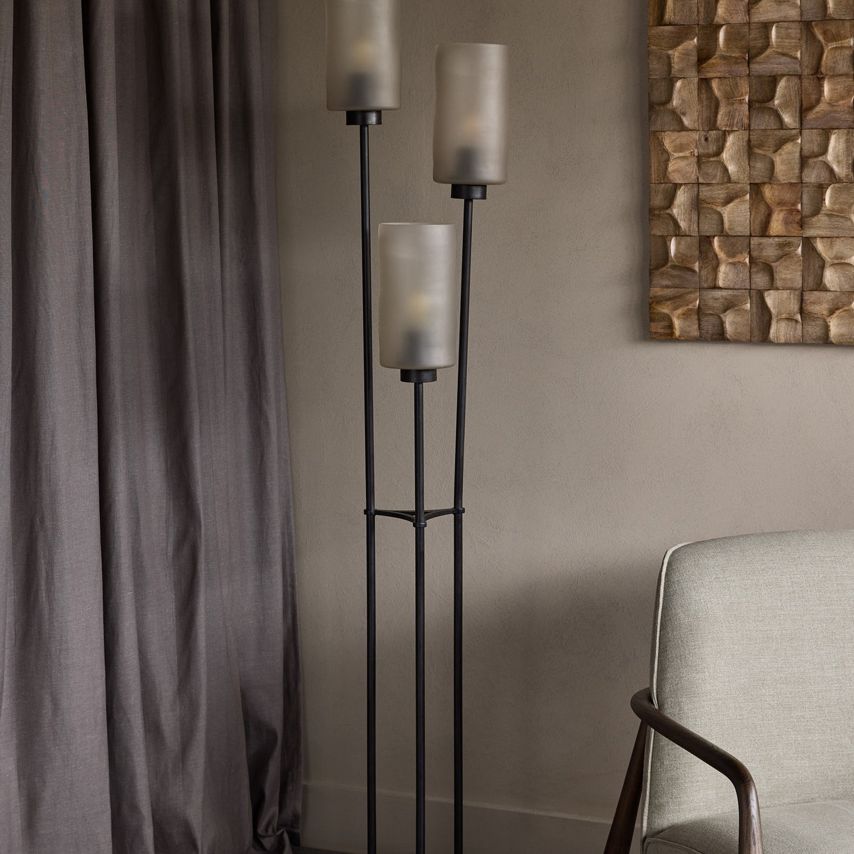 Libra Interiors Frosted Glass 3 Light Floor Lamp in black with tiered flute shades on slim iron stems, beside grey curtain and linen armchair.