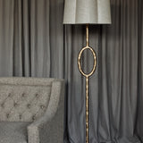 Libra Interiors Hammered Oval Gold Floor Lamp with iron stem, open oval detail and scalloped ivory linen shade beside a grey tufted armchair and curtains.