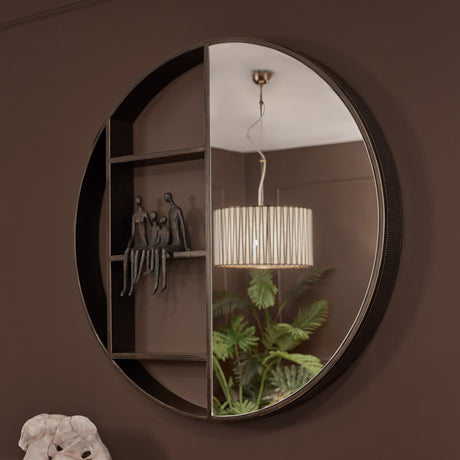 Libra Interiors Round Iron Shelved Wall Mirror in bronze, half mirrored glass and half three-compartment shelving with corrugated frame edge, on a brown wall.