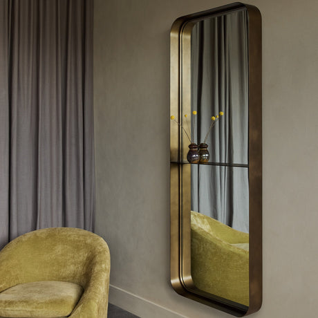 Libra Interiors Smoked Gold Iron Ledge Wall Mirror with rounded rectangular frame and integrated shelf holding small vases, mounted beside a yellow armchair.