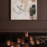 Libra Interiors 11 Light Branch Candelabra in bronze with lit tea lights in smoked glass holders, on a console below abstract art in a dining room.