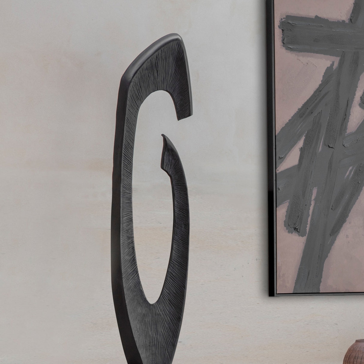 Libra Interiors textured cast aluminium abstract sculpture in matt black, with a sweeping hooked curve and open centre, beside a framed abstract artwork.
