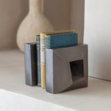 Libra Interiors Textured Cast Aluminium Bookends in grey holding vintage cloth-bound books, with geometric square form and hollowed centre on a pale shelf.