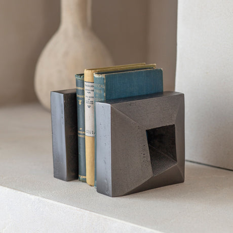 Libra Interiors Textured Cast Aluminium Bookends in grey holding vintage cloth-bound books, with geometric square form and hollowed centre on a pale shelf.