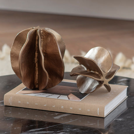 Libra Interiors Petal cast aluminium sculptures in antique brass, layered petal forms styled with a smaller companion piece on a book atop a marble surface.