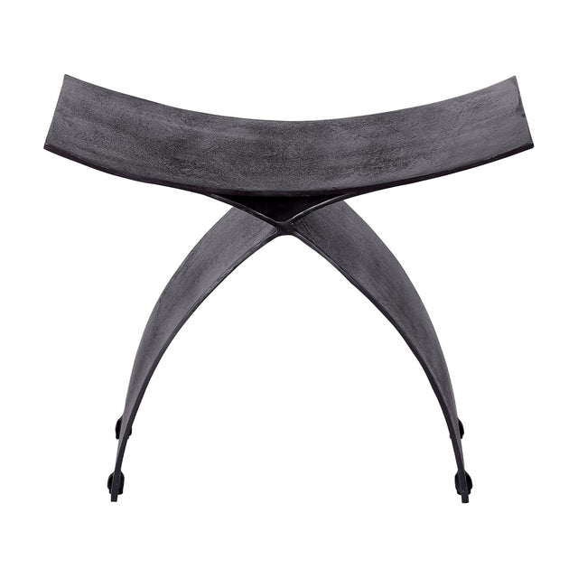 Libra Interiors Cast Aluminium Curved Stool in black, with arched crossed legs and a concave seat in raw textured finish, on a white background.