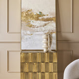 Libra Interiors Textured Brass 2 Door Cabinet in antique brass styled in a panelled room with a gold and white abstract artwork and cream vase on top.