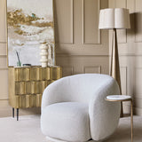 Libra Interiors Textured Brass 2 Door Cabinet in antique brass styled in a panelled living room with a bouclé chair, floor lamp and abstract artwork.
