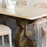 Libra Interiors Travertine Twin-Pedestal Dining Table in cream with a smooth stone top and sculptural etched antique brass pedestal, styled with linen chairs.