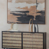 Libra Interiors Bone Inlay sideboard with black frame and ivory raised-pattern doors, styled with a vase, sculptures and book beneath abstract art.