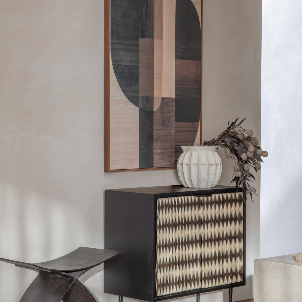 Libra Interiors Bone Inlay 2 Door Cabinet in black with ridged ivory bone front, styled with a white vase and dried foliage beneath abstract wall art.