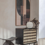 Libra Interiors Bone Inlay 2 Door Cabinet in black with ridged ivory bone front, styled with a white vase and dried foliage beneath abstract wall art.