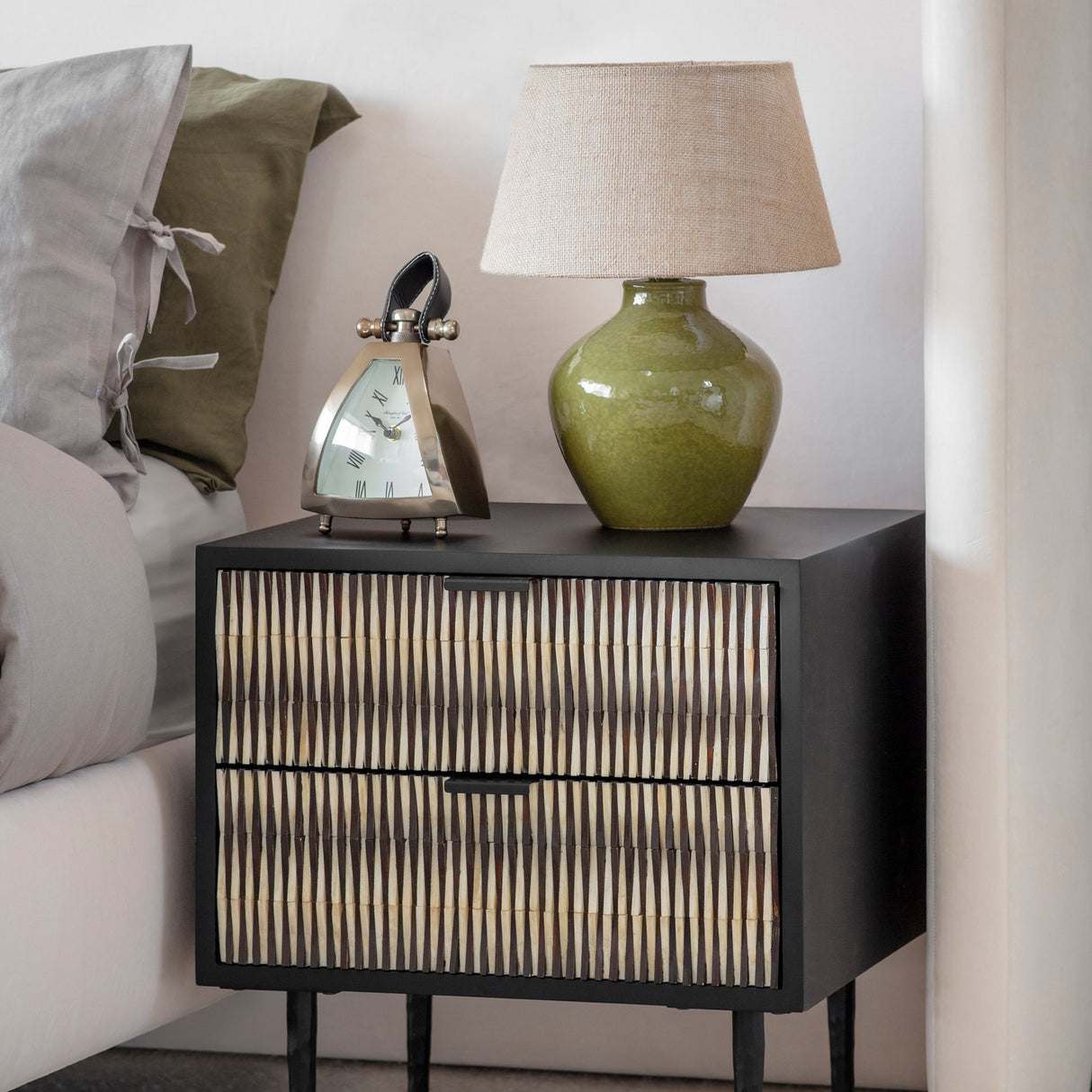 Libra Interiors Bone Inlay 2-Drawer Bedside Table in black with ivory patterned drawer fronts, styled beside a bed with a green lamp and silver clock.