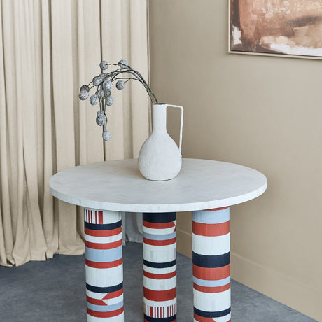 Libra Interiors Bone Inlay Round Dining Table with cream top and three legs in terracotta, black, ivory and grey stripes, styled with a white vase.