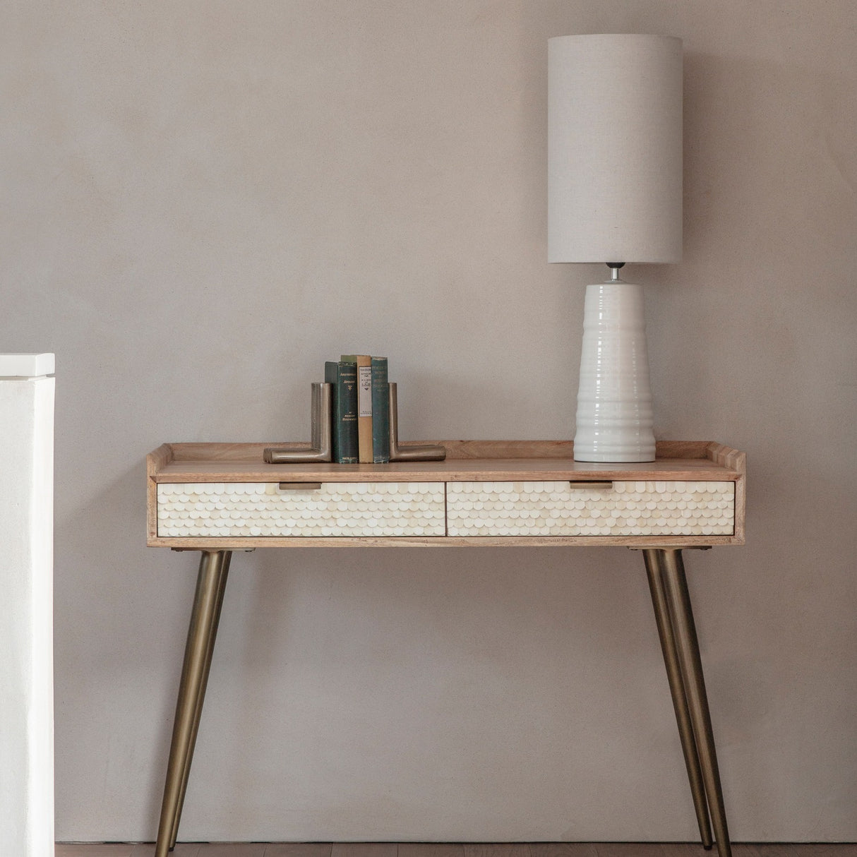 Libra Interiors Scalloped Bone Inlay Mango Wood Desk in cream styled with a white lamp, books and bookends against a neutral wall.
