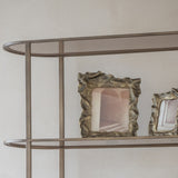 Libra Interiors woven-effect cast aluminium photo frames in antique brass, displayed upright on a metal shelving unit against a neutral wall.