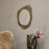 Libra Interiors Honeycomb cast aluminium wall mirror in gold with organic openwork frame, hung on a neutral wall above a bronze vase holding a pale bloom.