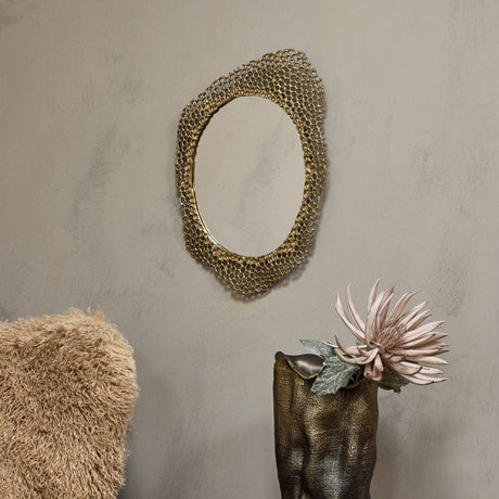 Libra Interiors Honeycomb cast aluminium wall mirror in gold with organic openwork frame, hung on a neutral wall above a bronze vase holding a pale bloom.