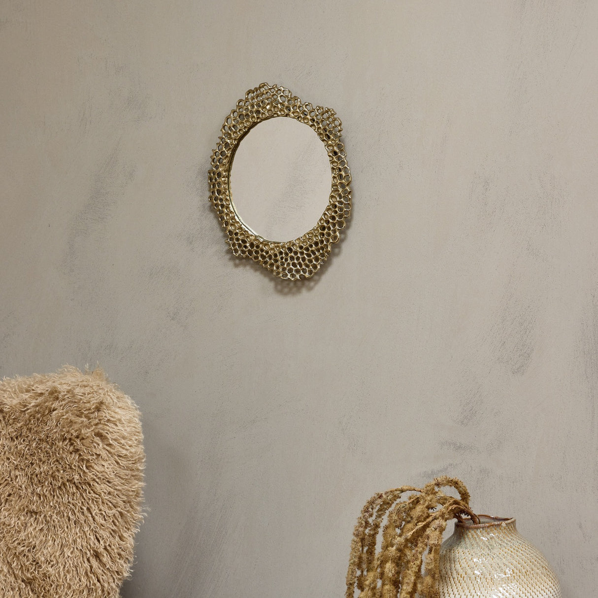 Libra Interiors Honeycomb cast aluminium wall mirror in gold with sculpted openwork frame, styled on a neutral wall above a textured cushion and ceramic vase.
