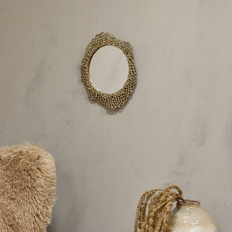 Libra Interiors Honeycomb cast aluminium wall mirror in gold with sculpted openwork frame, styled on a neutral wall above a textured cushion and ceramic vase.