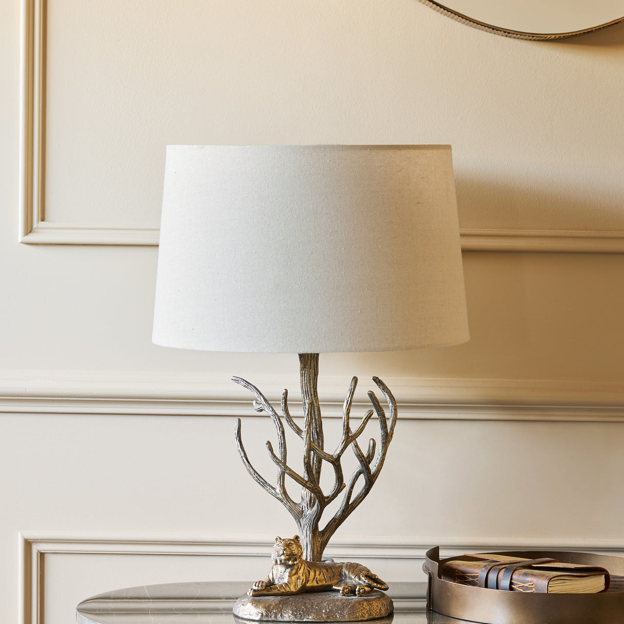 Libra Interiors Antiqued Brass Tiger Table Lamp with resting tiger and bare branch base under a cream tapered shade, on a side table by panelled wall.